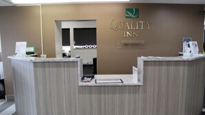 A reception desk at Quality Inn with a sign above it, a counter with a nameplate, and a mirror on the wall. - Quality Inn Mount Pleasant (Mount Pleasant)