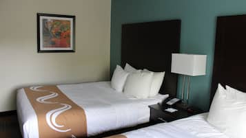 A hotel room with two beds, a nightstand with a lamp, a phone, and a framed picture on the wall.