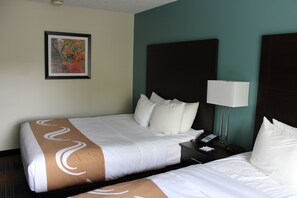 A hotel room with two beds, a nightstand with a lamp, a phone, and a framed picture on the wall.