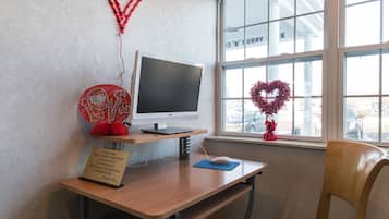 A computer desk with a monitor, a sign, and a heart-shaped decoration by a window.