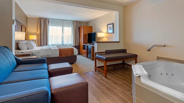 A hotel room with a large bed, a sofa, a desk, a TV, and a bathtub. - Comfort Inn & Suites Wilkes Barre - Arena (Wilkes-Barre)