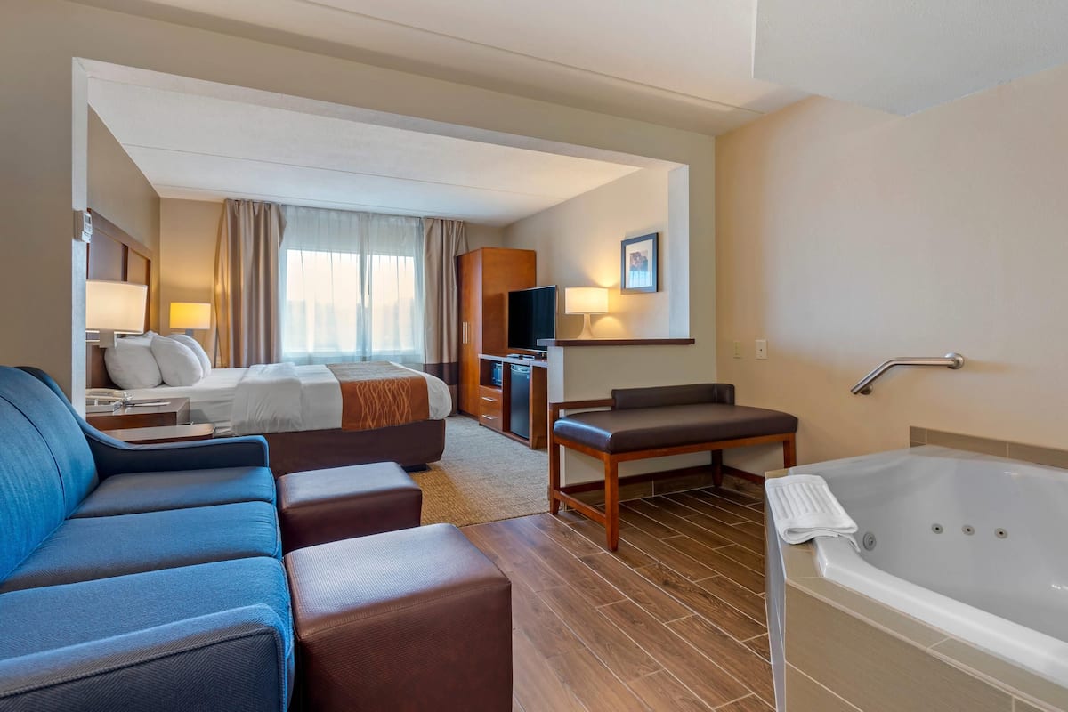 A hotel room with a large bed, a sofa, a desk, a TV, and a bathtub.