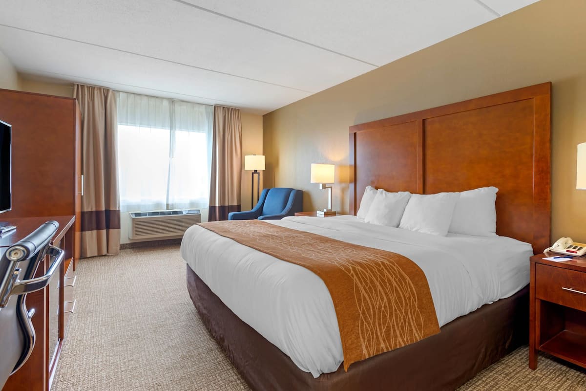 A hotel room with a large bed, a desk with a chair, a television, and a window with curtains.