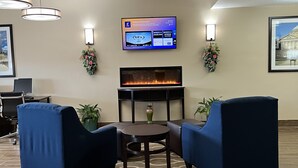 A lobby area with a flat-screen TV displaying a welcome message, two blue armchairs, a small round table, and a decorative fireplace. - Comfort Inn & Suites Wilkes Barre - Arena (Wilkes-Barre)