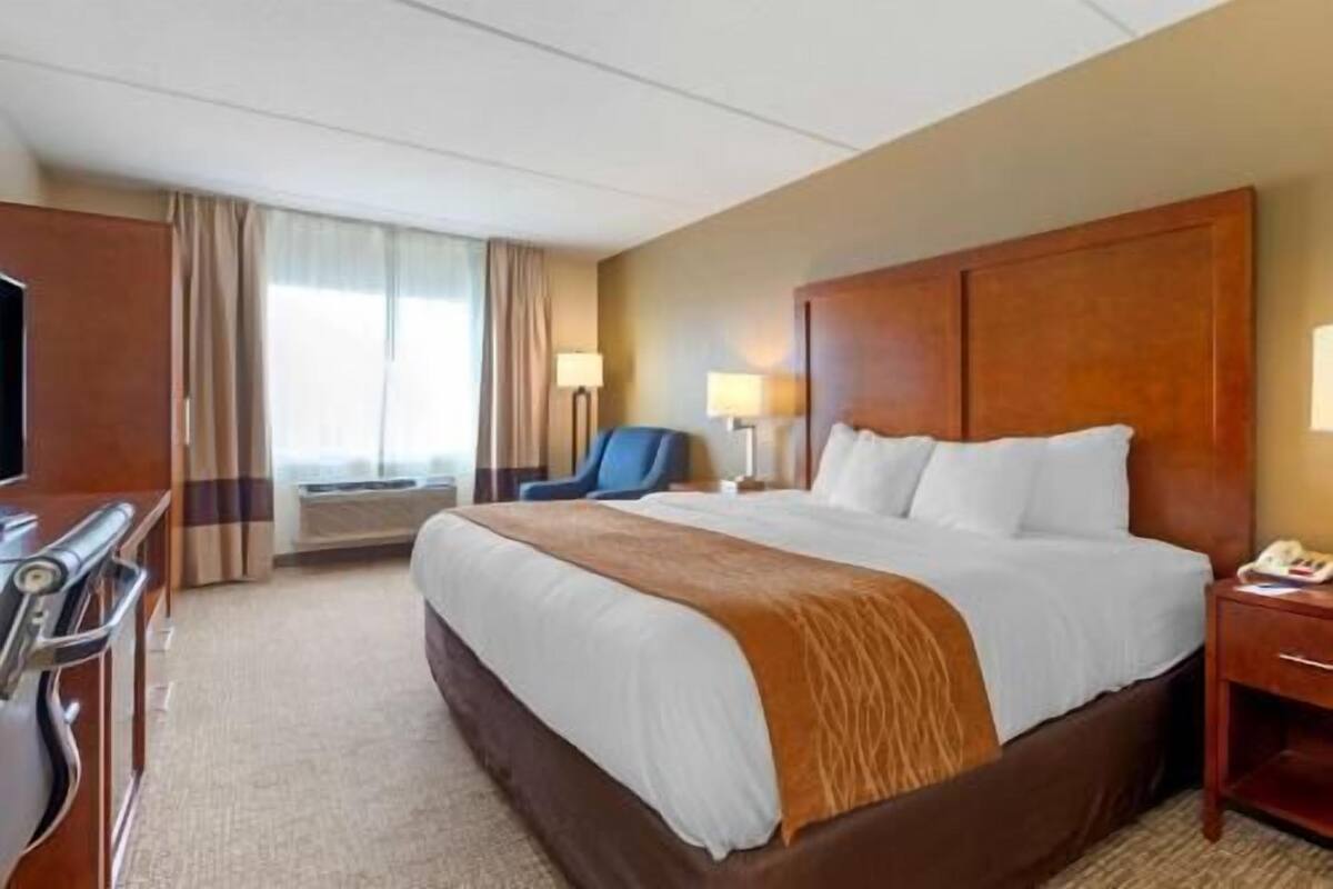 A hotel room with a large bed, a desk, a chair, and a TV.