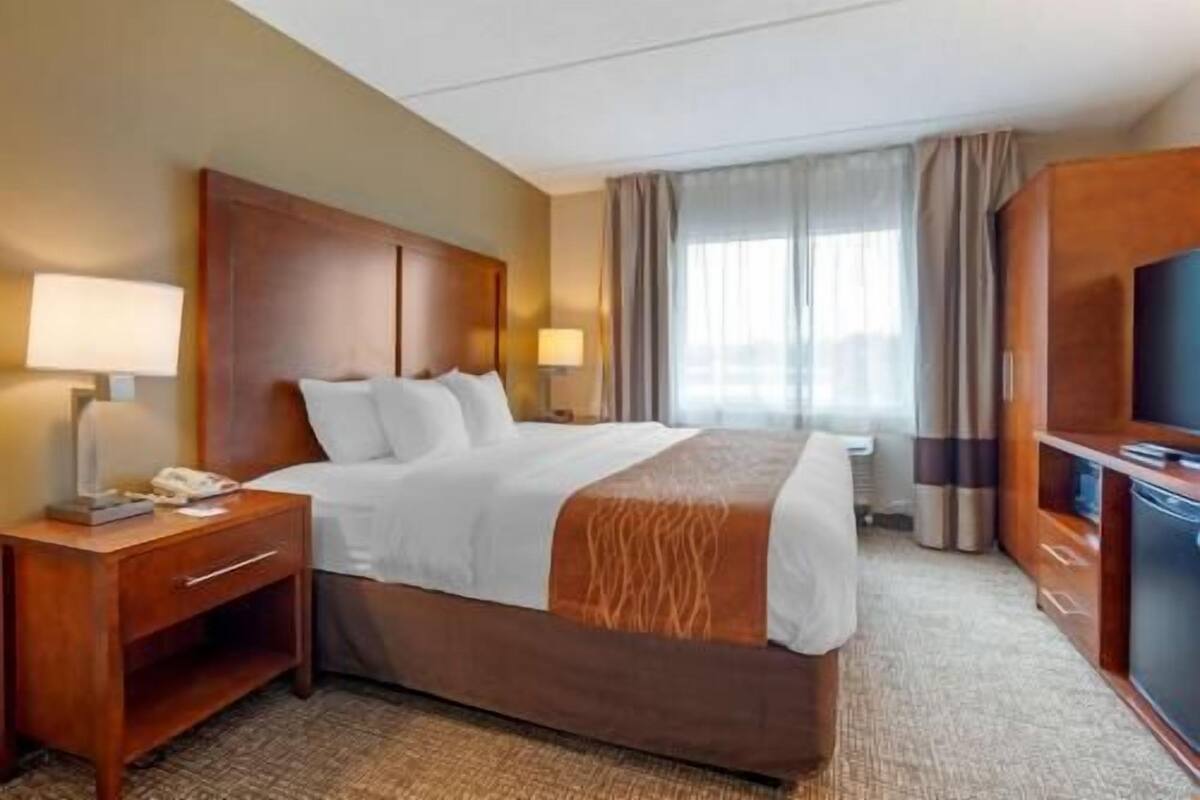 A hotel room with a bed, two bedside tables, a TV, and a window with curtains.