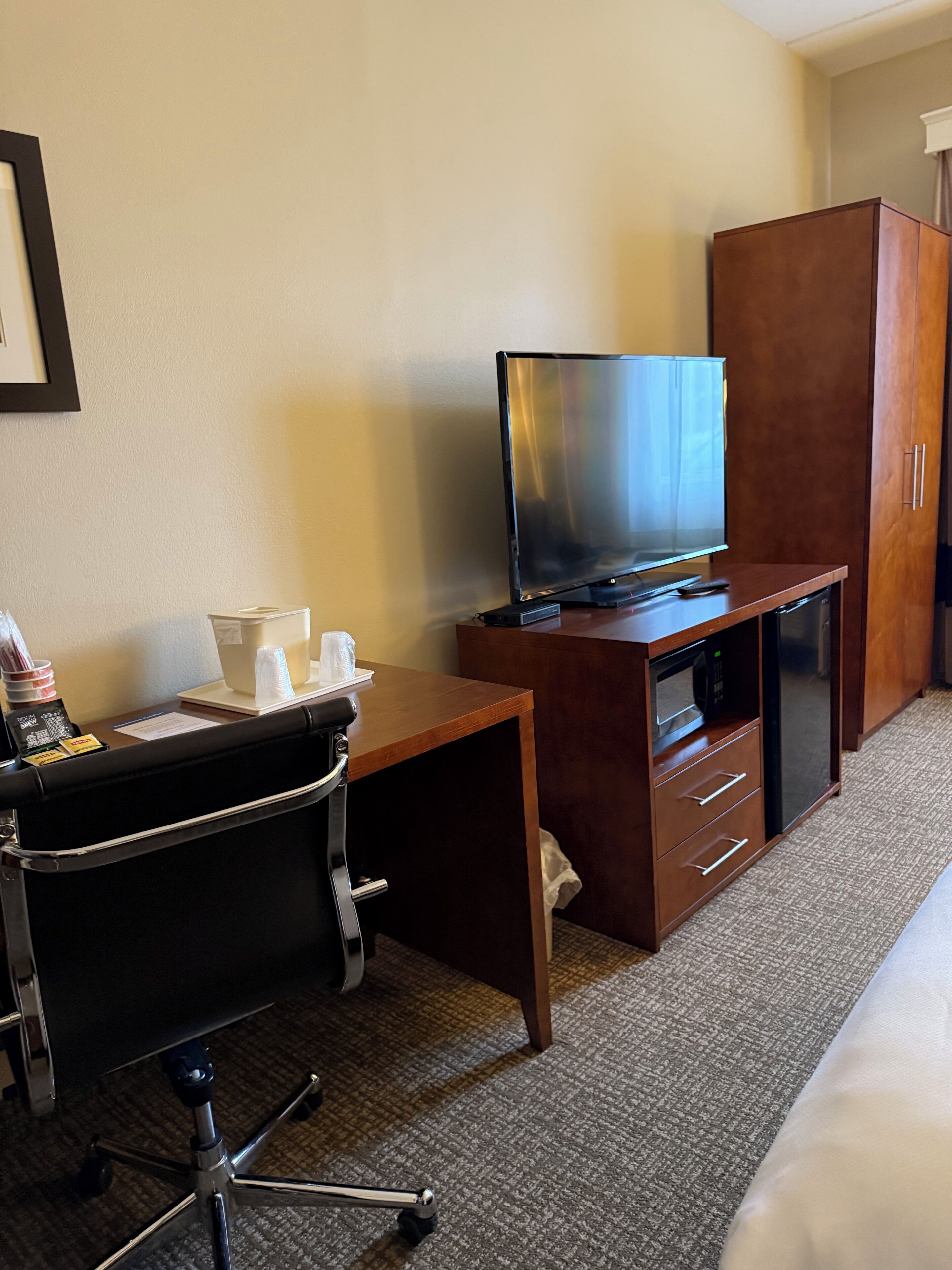 A hotel room with a desk, a television, a wardrobe, and a bed.