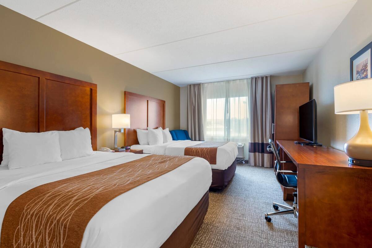 A hotel room with two beds, a desk, a TV, and a lamp.