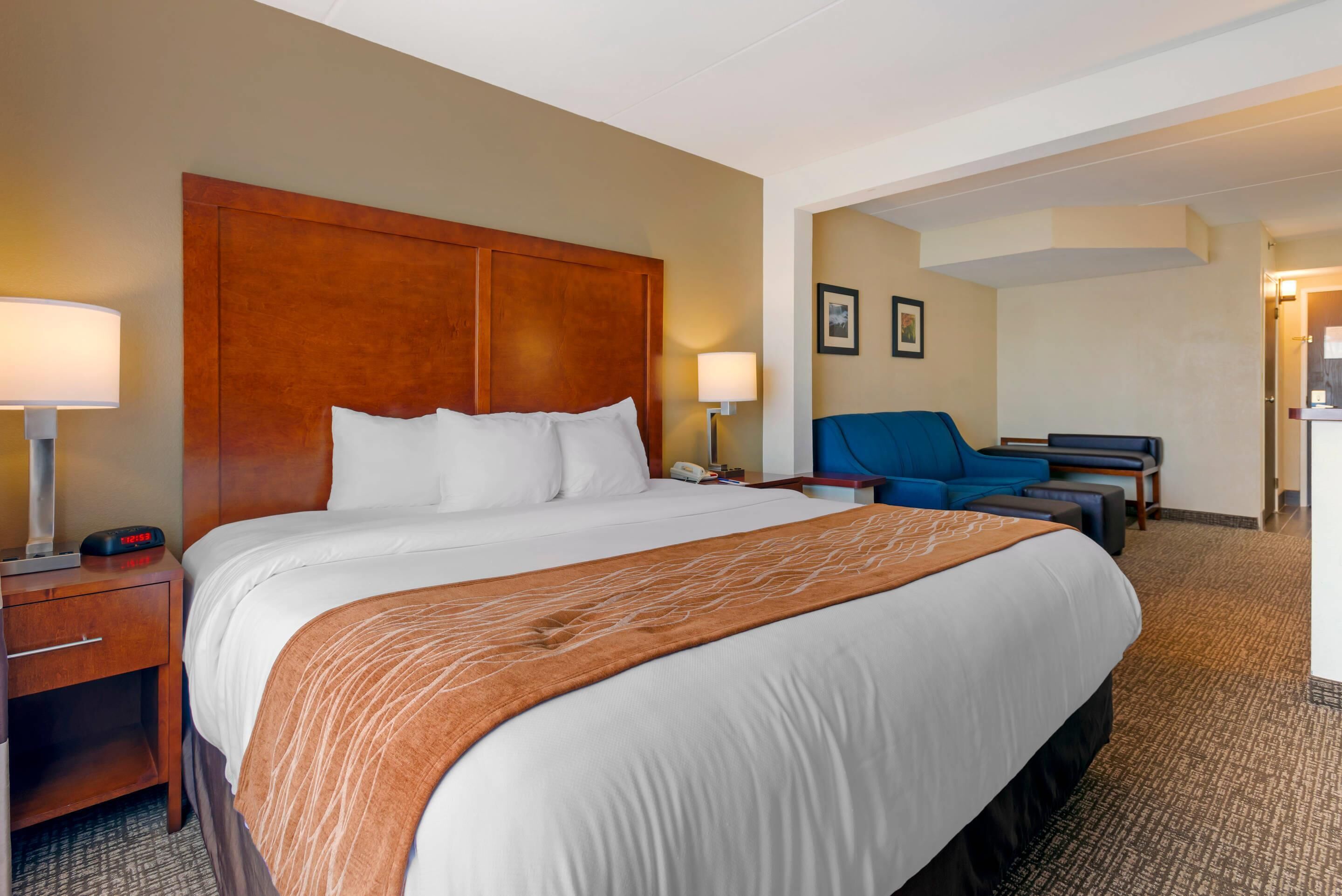 A hotel room with a large bed, a desk with a chair, a lamp, and a wall-mounted phone.