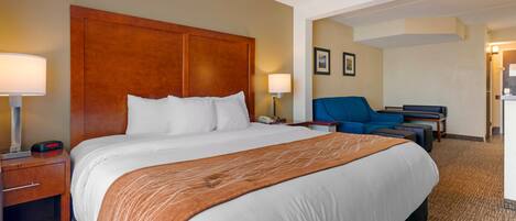 A hotel room with a large bed, a desk with a chair, a lamp, and a wall-mounted phone.