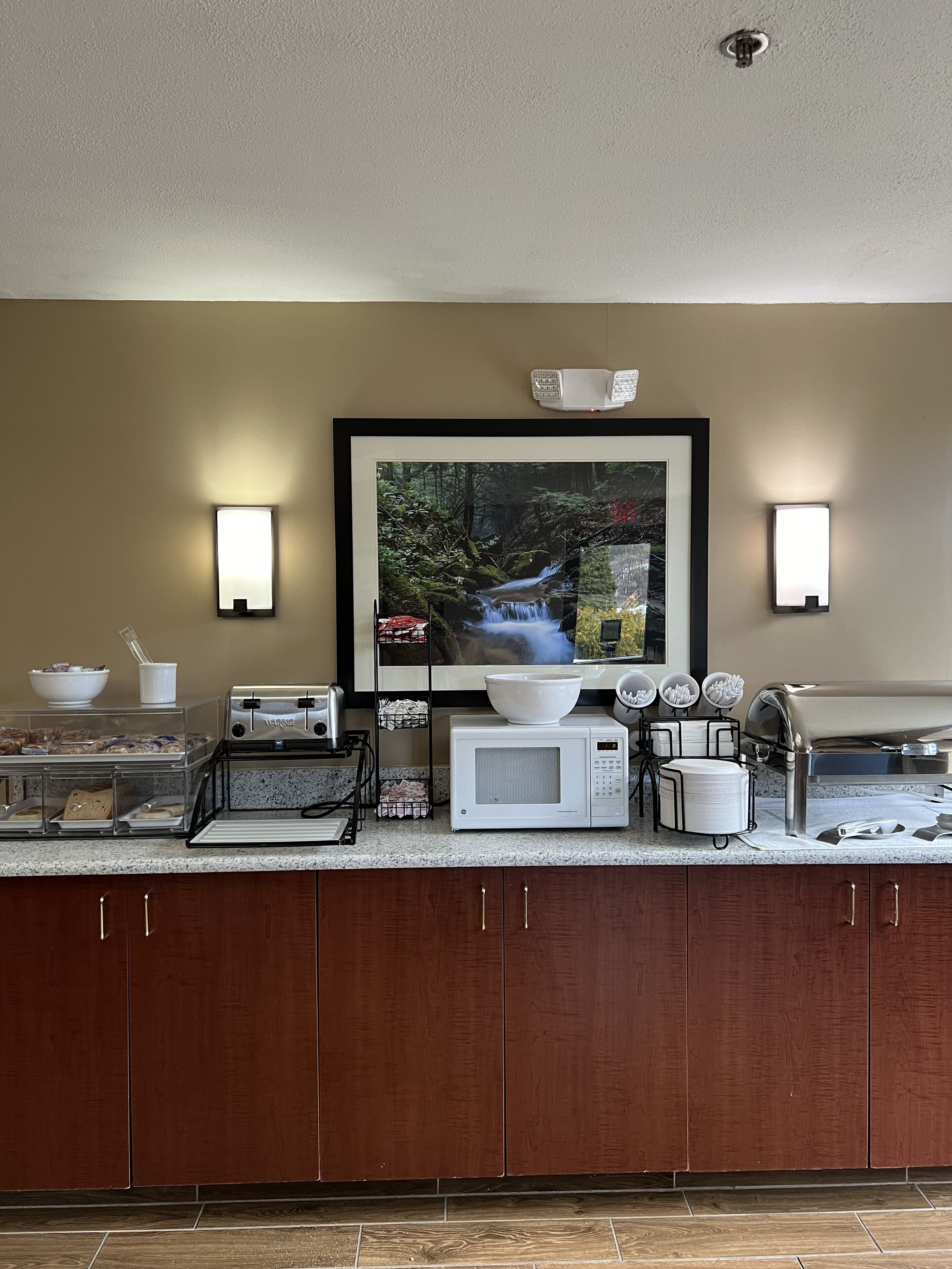A kitchen with a framed picture of a waterfall, a microwave, a toaster, and a coffee maker.