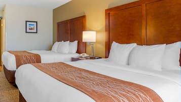 A hotel room with two beds, a wooden headboard, a bedside lamp, a phone, and a framed picture on the wall.