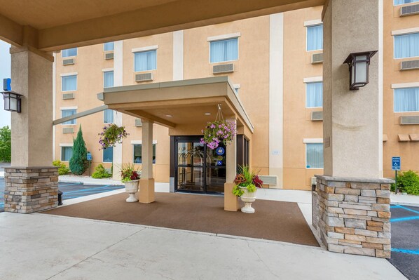 A hotel entrance with a covered walkway, potted plants, and a clear handicap parking sign.