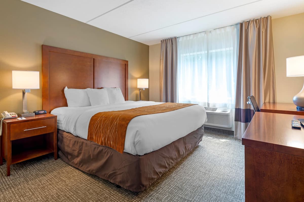 A hotel room with a large bed, two bedside tables with lamps, a desk, and a window with curtains.