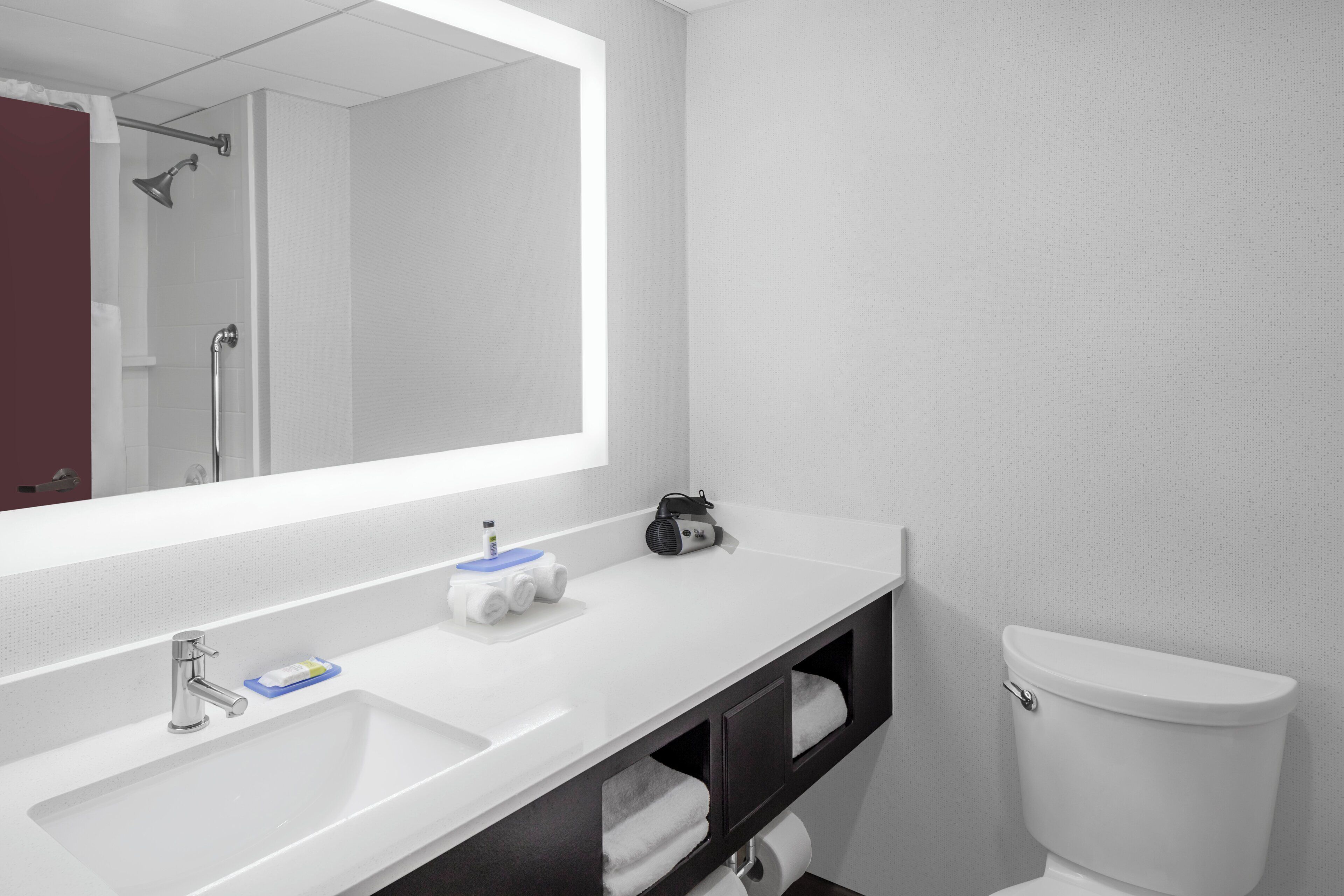 A modern bathroom with a large mirror, two sinks, a shower, and a toilet.
