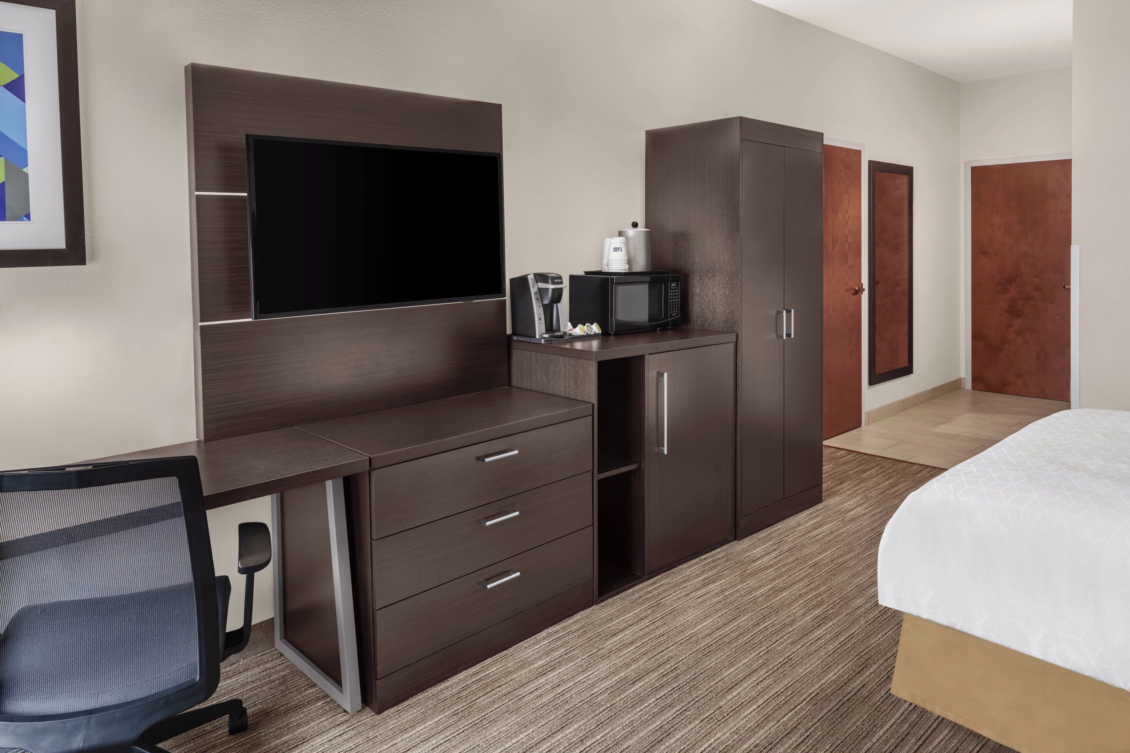 Habitación de hotel con cama, escritorio con silla, televisor, armario y microondas.