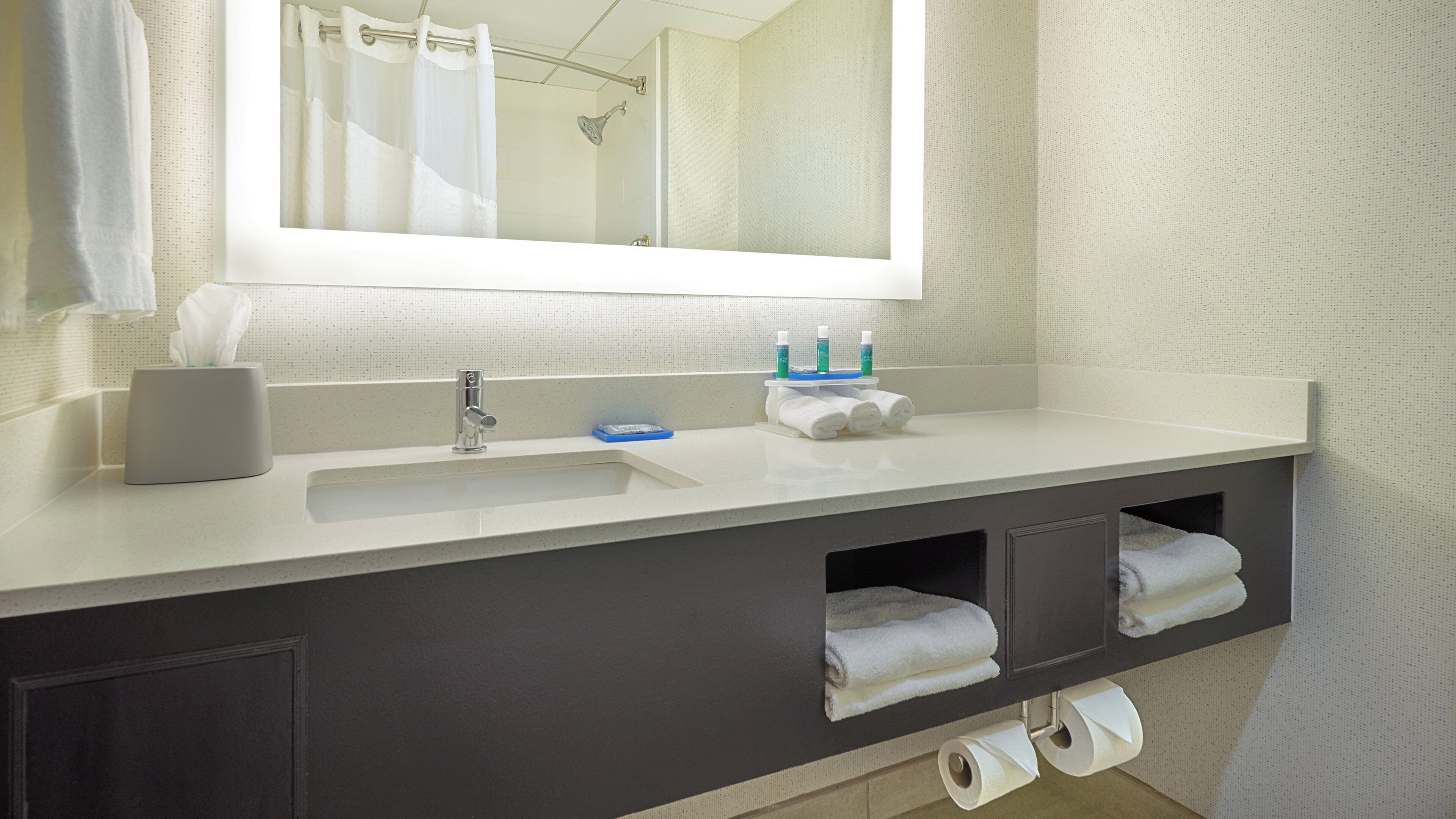 A bathroom with a white sink, a mirror, a towel rack, and a shelf with toiletries.