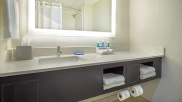 Un baño con un lavamanos blanco, un espejo, un perchero para toallas y un estante con artículos de aseo.