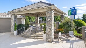 A covered outdoor seating area with stone pillars, a patio, and a sign for Holiday Inn Express & Suites. - Holiday Inn Express & Suites Asheville SW - Outlet Ctr Area by IHG (Asheville)