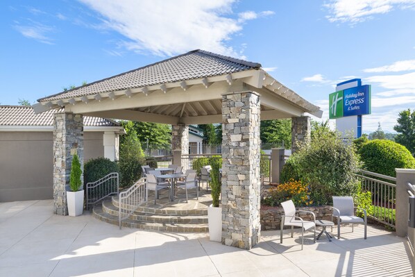 Un espace extérieur aménagé, abrité et doté de piliers en pierre, ainsi qu’une terrasse et une enseigne indiquant « Holiday Inn Express & Suites ».