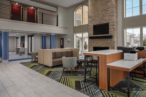 A spacious lobby with a high ceiling, a seating area with a sofa and chairs, a coffee station, and a fireplace.