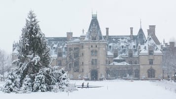 A large, historic building with multiple chimneys and a snow-covered lawn.