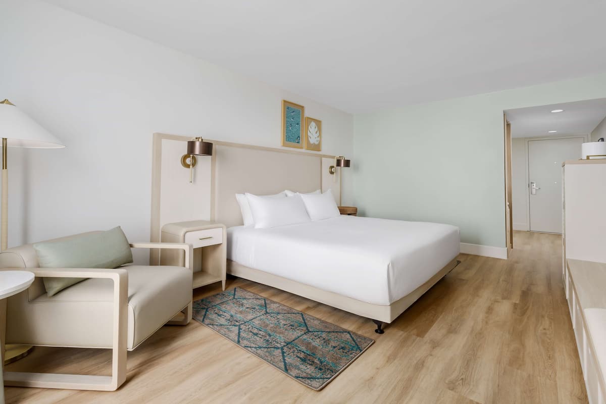 A modern hotel room with a bed, a sofa, a nightstand, and a lamp.
