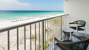 A balcony with wicker chairs and a table overlooking a beach with umbrellas. - Beal House Fort Walton Beach, Tapestry Collection by Hilton (Fort Walton Beach)