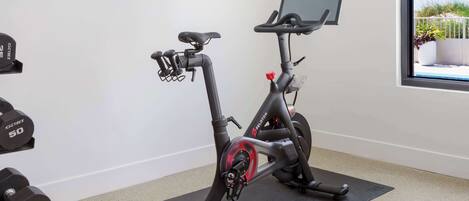 Una bicicleta estática con pantalla, mancuernas y una ventana con vistas.