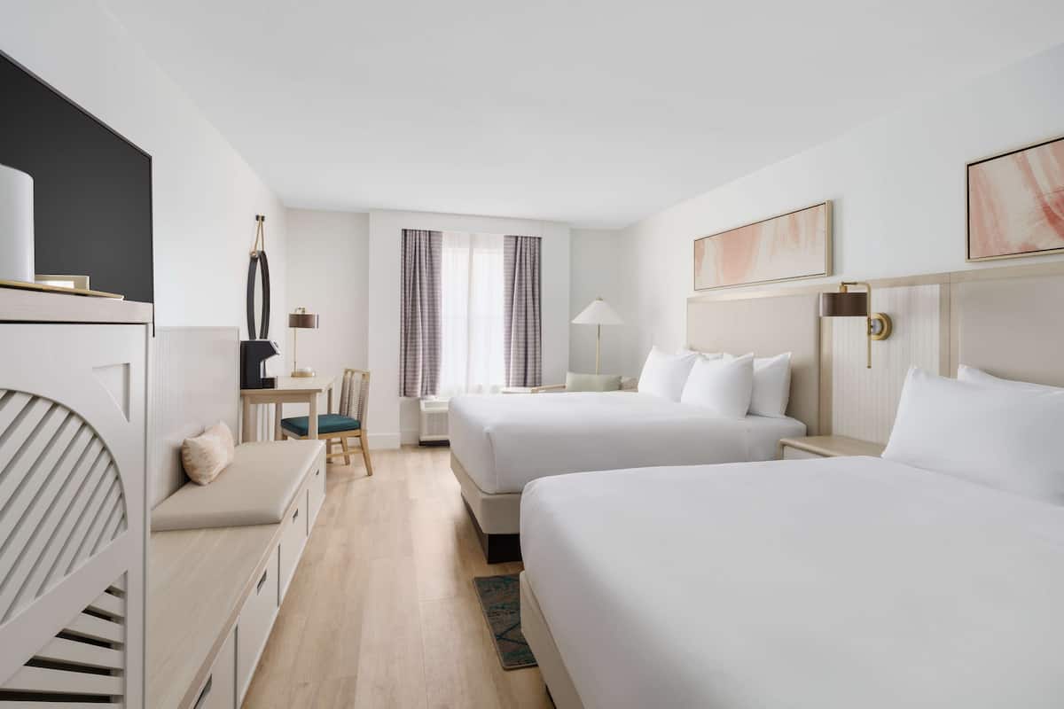 A hotel room with two beds, a desk, a chair, and a window with curtains.