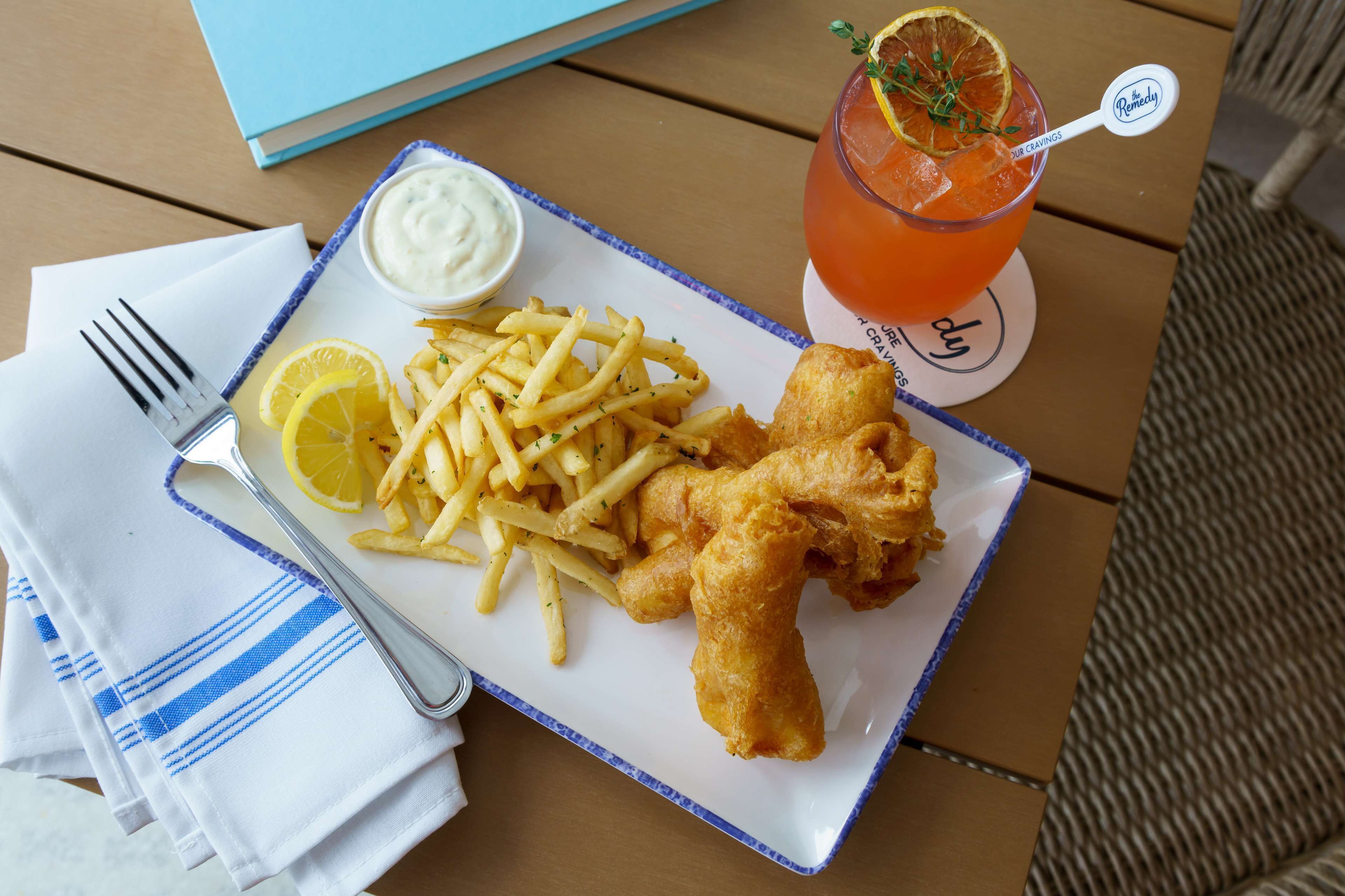 A plate of fish and chips with lemon wedges, a side of tartar sauce, and a glass of a beverage with a lemon garnish.