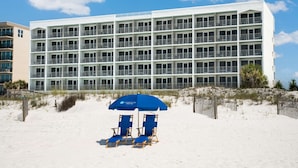 A multi-story hotel with a white facade and balconies. There are two blue beach chairs under a blue umbrella in the foreground. - Beal House Fort Walton Beach, Tapestry Collection by Hilton (Fort Walton Beach)