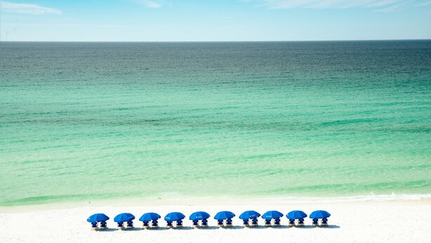 A beach with a row of blue umbrellas and beach chairs. - Beal House Fort Walton Beach, Tapestry Collection by Hilton (Fort Walton Beach)