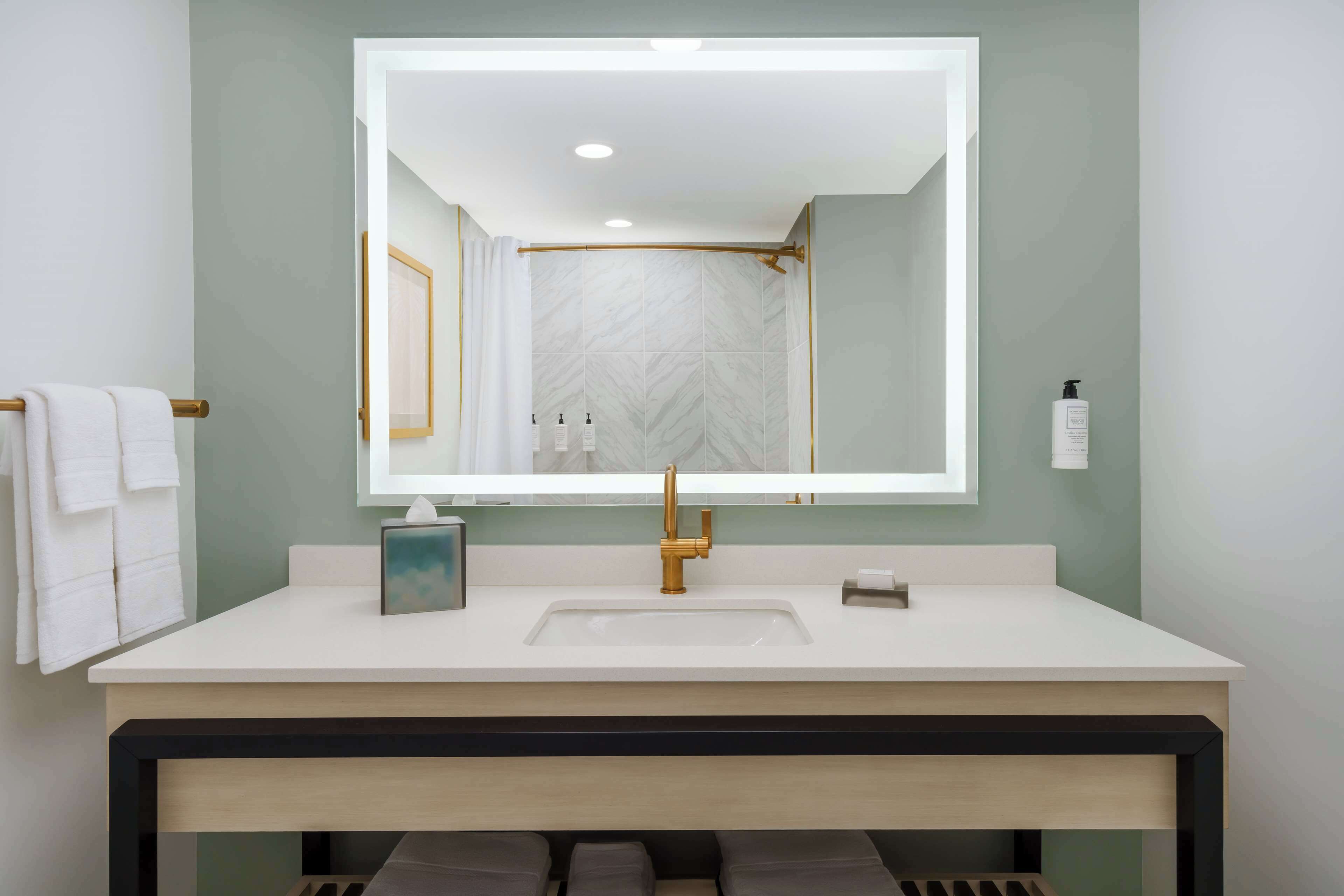 Un baño moderno con un espejo grande, lavamanos blanco y un toallero con toallas blancas.