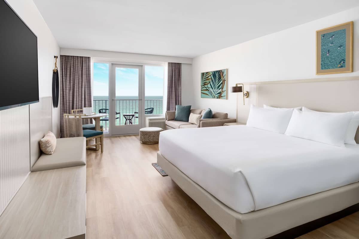 A hotel room with a large bed, a seating area with a table and chairs, and a balcony with a view.