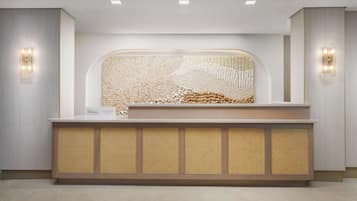 A reception desk with a woven tapestry backdrop, a sign indicating a Hilton hotel, and two wall-mounted light fixtures.