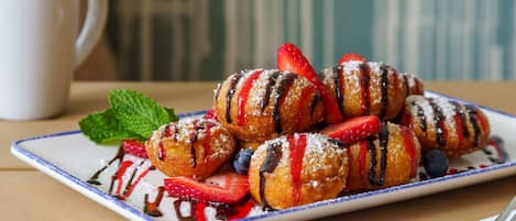 Un plato de pasteles con fresas y arándanos, una taza blanca y una servilleta con un tenedor sobre una mesa de madera.