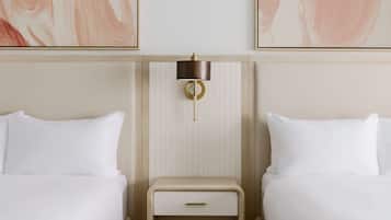 A hotel room with two beds, a bedside table with a lamp, and abstract artwork on the walls.