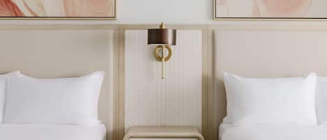 A hotel room with two beds, a bedside table with a lamp, and abstract artwork on the walls.