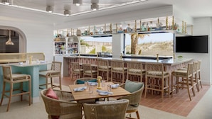A modern outdoor bar area with wicker furniture, a bar counter, and a television screen. - Beal House Fort Walton Beach, Tapestry Collection by Hilton (Fort Walton Beach)