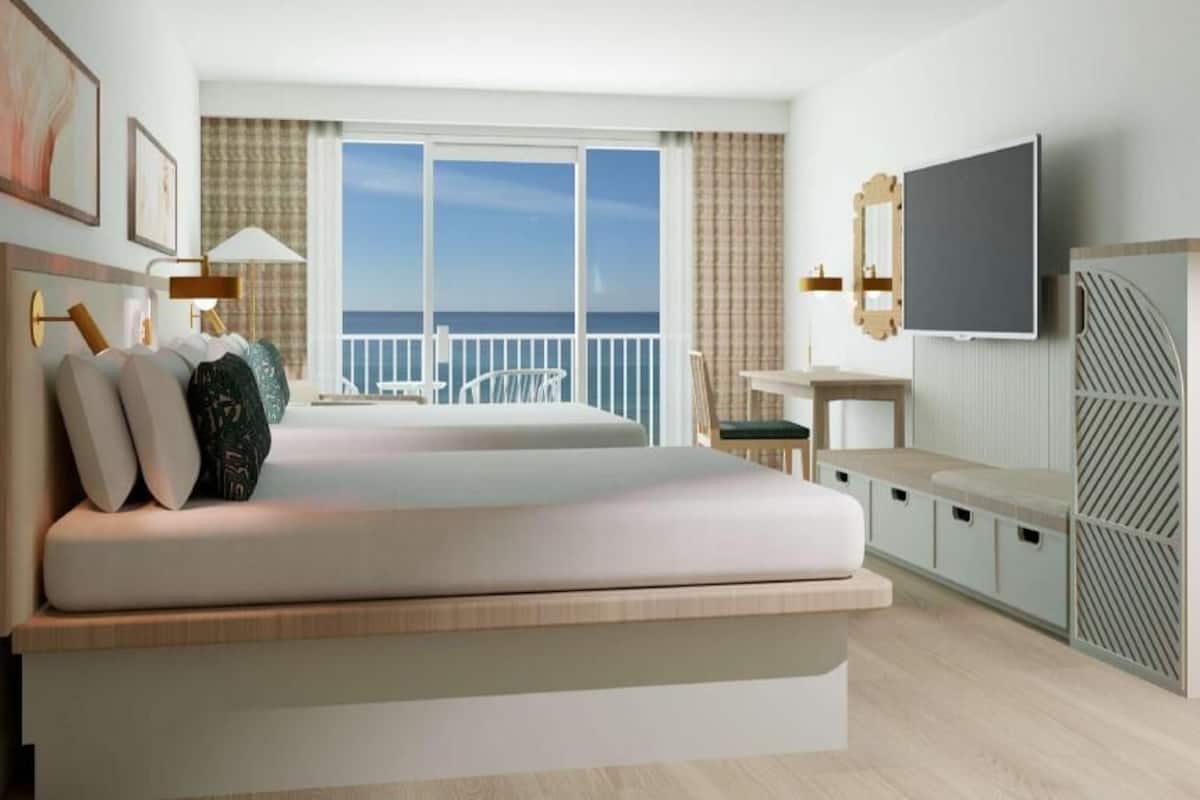 Una habitación de hotel moderna con una cama grande, televisor, escritorio y balcón con vistas al mar.