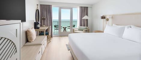 Una camera d'albergo con un letto grande, una scrivania con una sedia, un tavolino con sedie e un balcone vista mare.