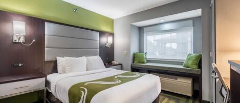 A hotel room with a bed, bedside table, lamp, window seat, and a view of the outside.
