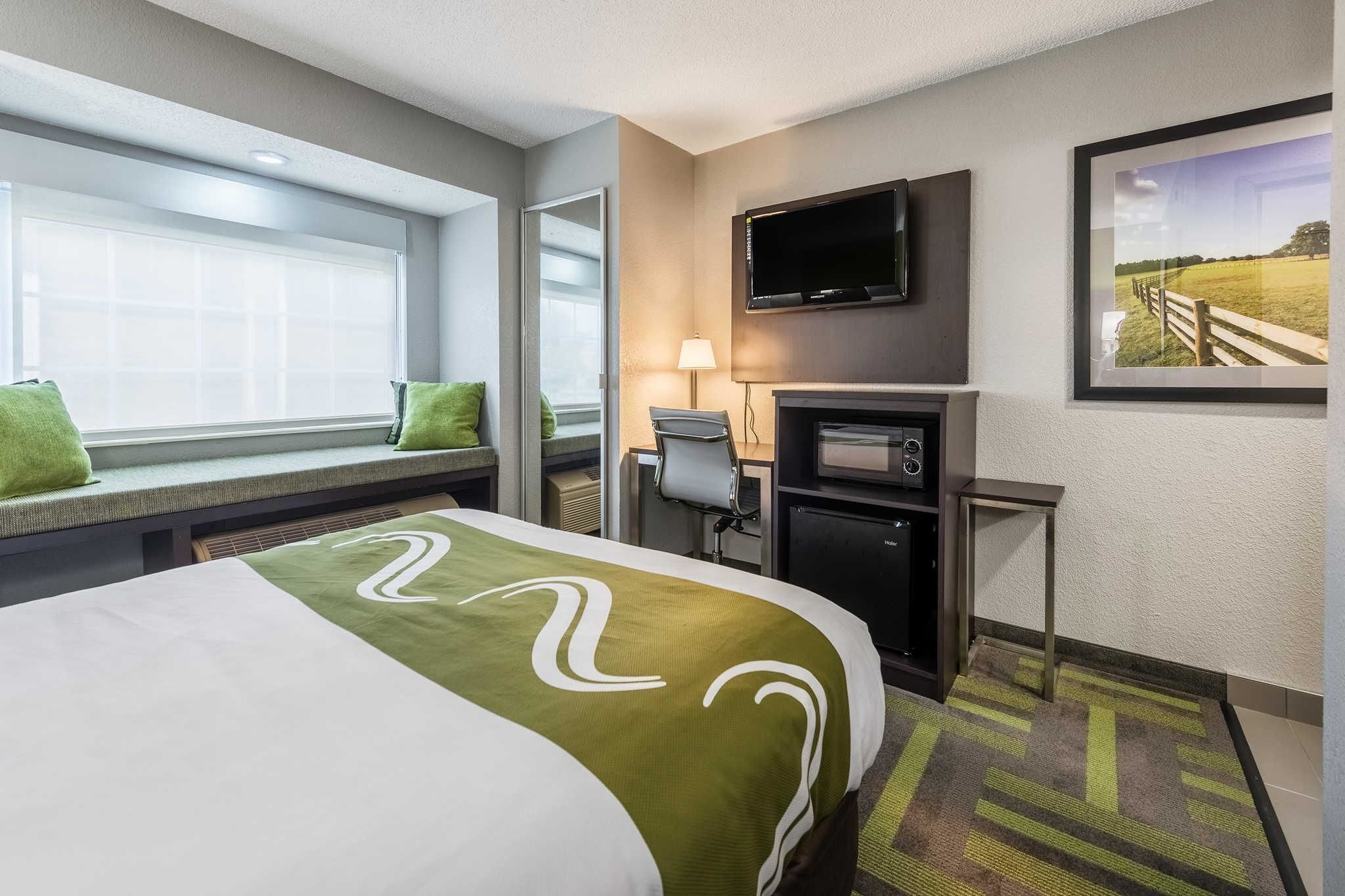 A hotel room with a bed, a desk, a television, a fireplace, and a window with blinds.