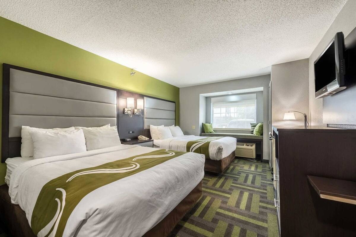 A hotel room with two beds, a window, a TV, and a desk.