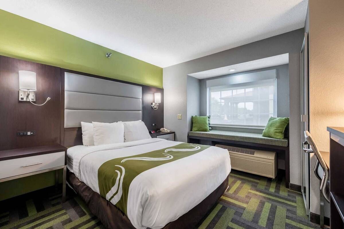 A hotel room with a bed, bedside tables, a window with a view, and a built-in heater.