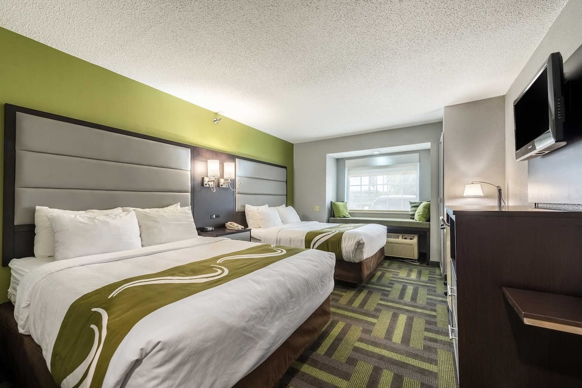 A hotel room with two beds, a desk, a TV, and a window with a view.
