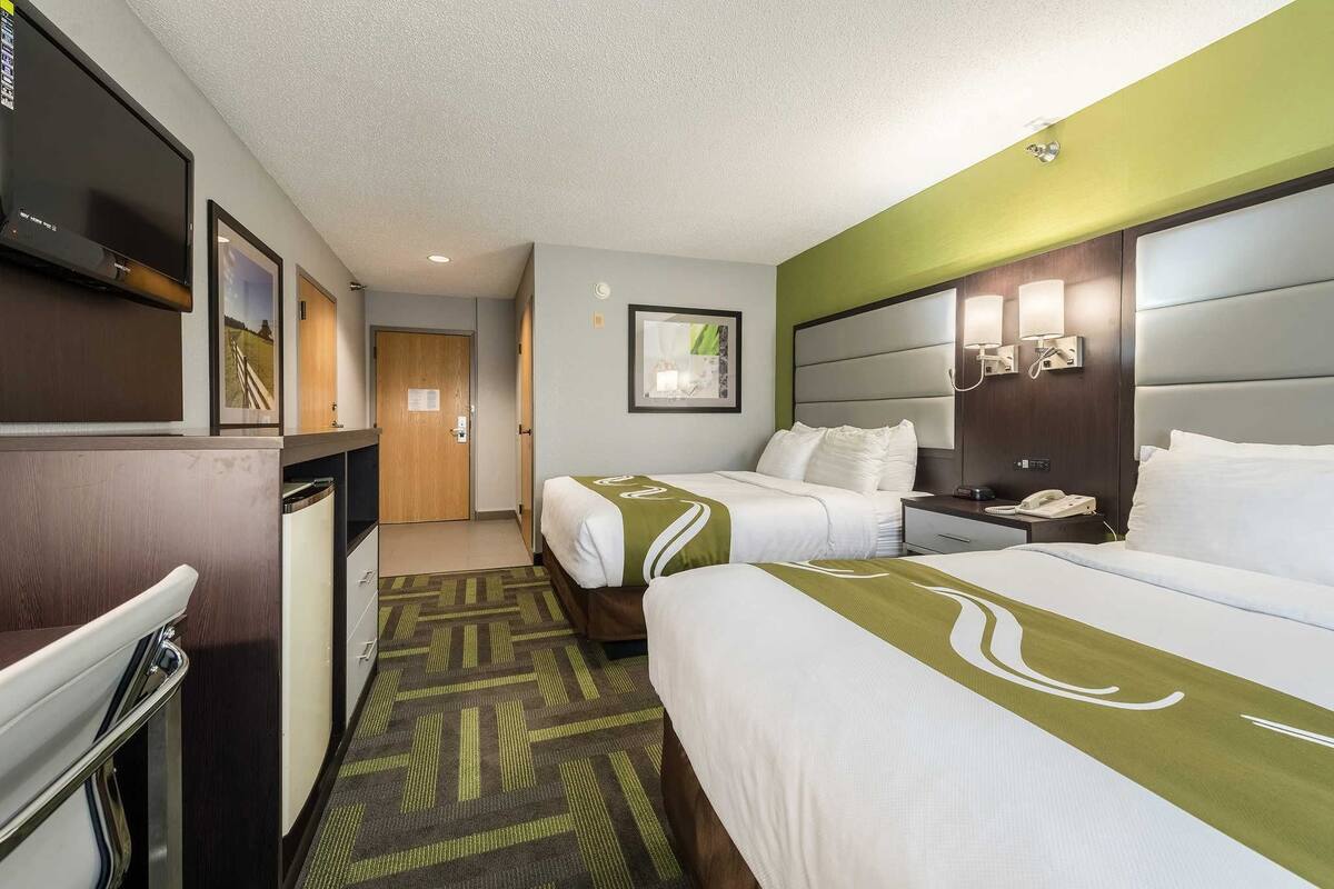 A hotel room with two beds, a desk, a television, and a bathroom.
