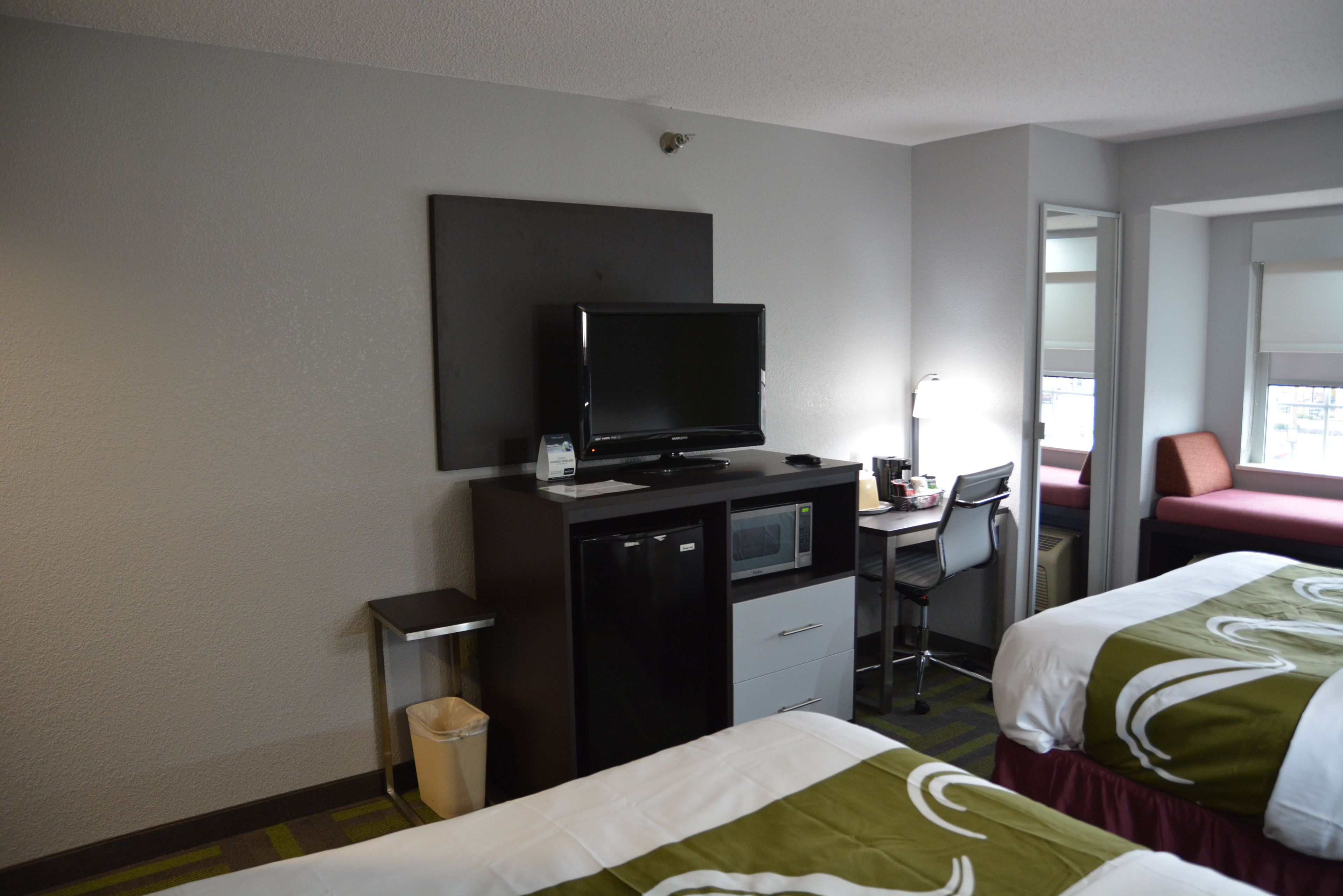 Quarto de hotel com duas camas, uma mesa de trabalho com computador, televisão e micro-ondas.