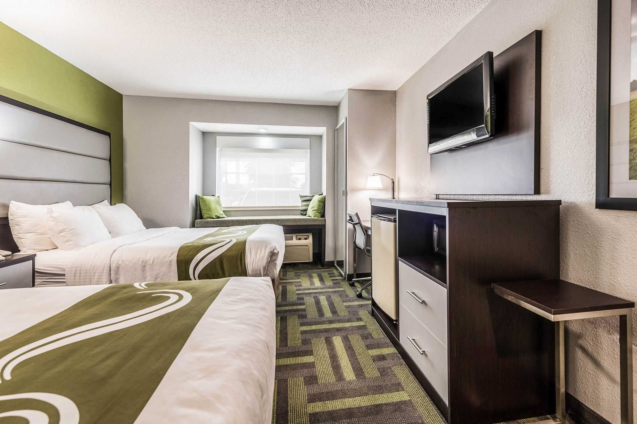 A hotel room with two beds, a desk, a television, and a window with a view.